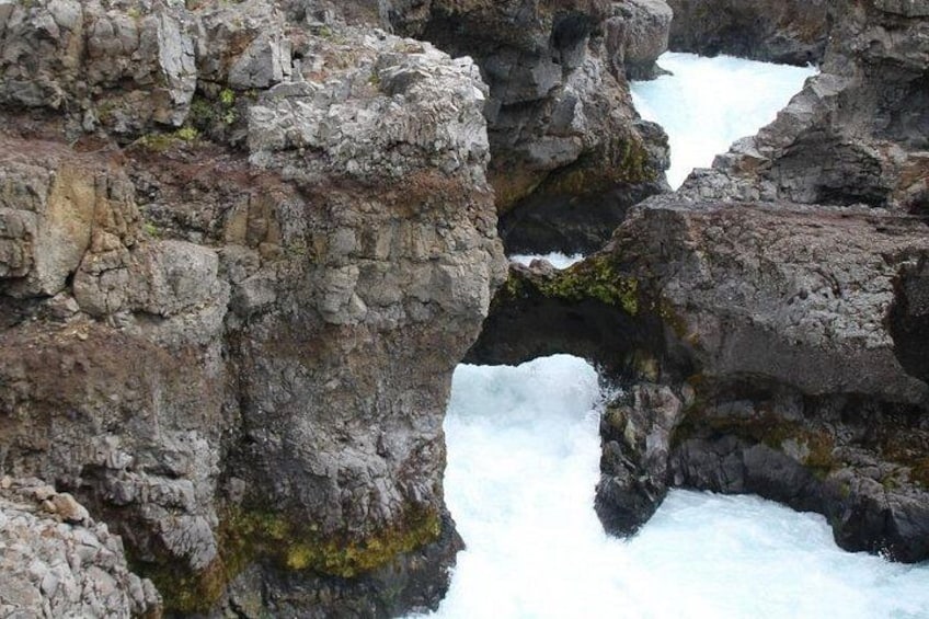 Un paisaje rocoso con una cascada que fluye a través de un arco natural. 4
