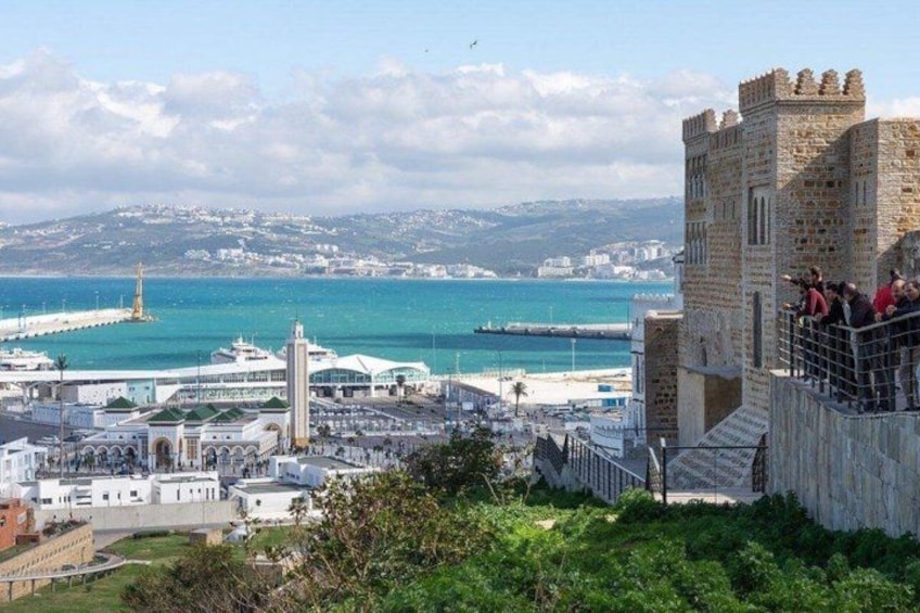 A coastal cityscape with a prominent castle, a lighthouse, and a modern building complex. 3