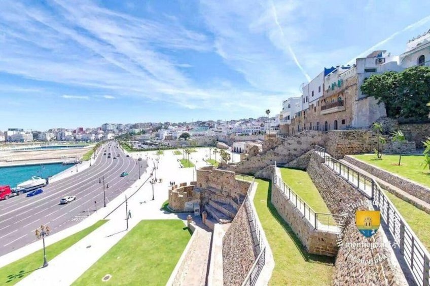 A coastal cityscape with a historic fort, a road leading to the sea, and modern buildings. 5