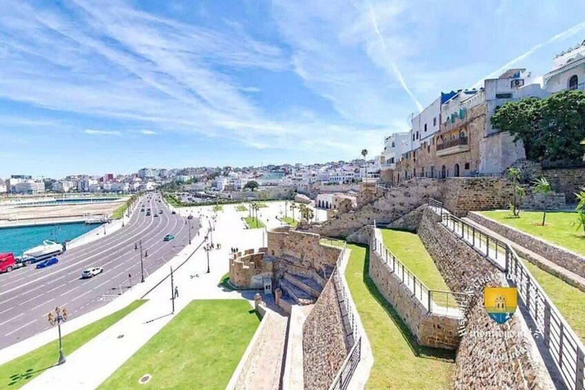 Un paisaje urbano costero con una fortaleza histórica, una carretera que lleva al mar y edificios modernos. 5