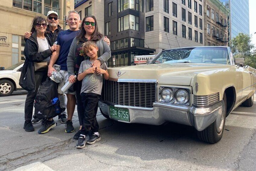 A vintage car parked on a street with a family posing in front. 5