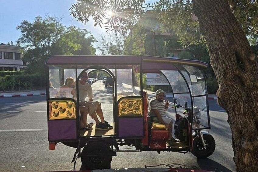 A tuk-tuk parked on a road with passengers inside. 3