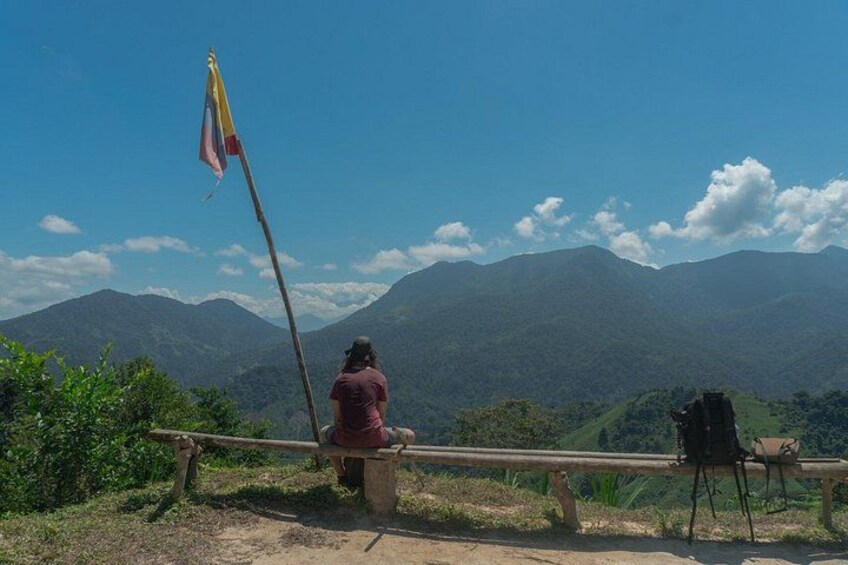 A person sitting on a bench with a flagpole in a mountainous landscape. 3