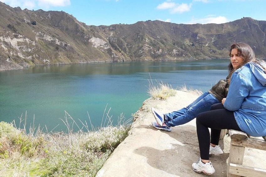 A person sitting on a bench by a lake with mountains in the background. 2