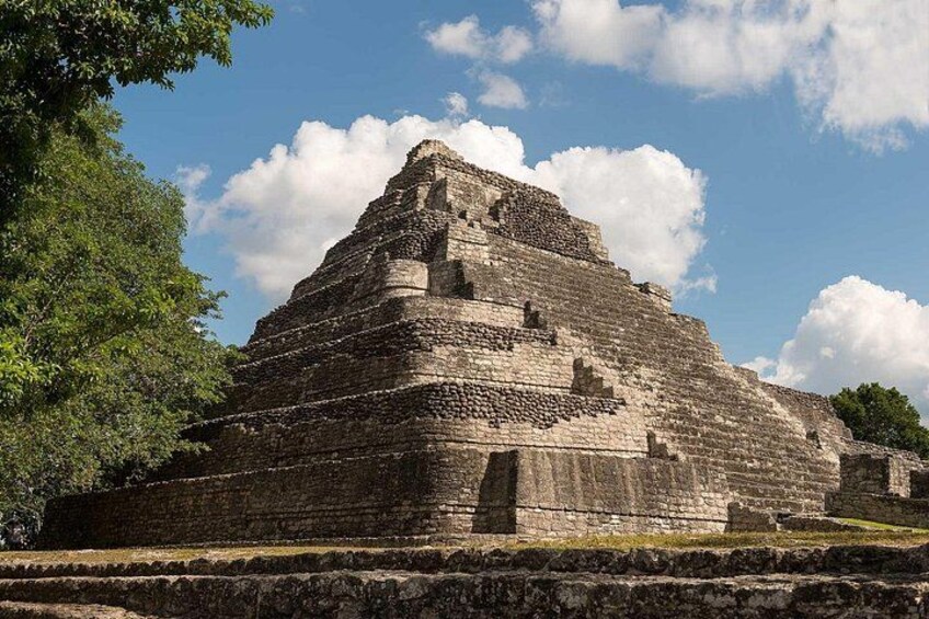 Een grote, oude piramide met meerdere niveaus, omringd door bomen en onder een heldere hemel. 2