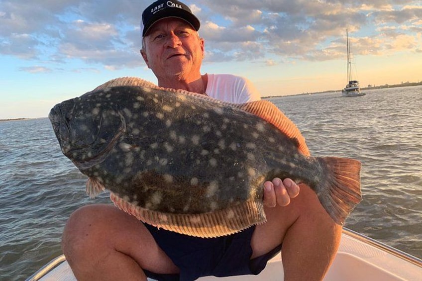 A person holding a large fish on a boat with a sailboat in the background. 1