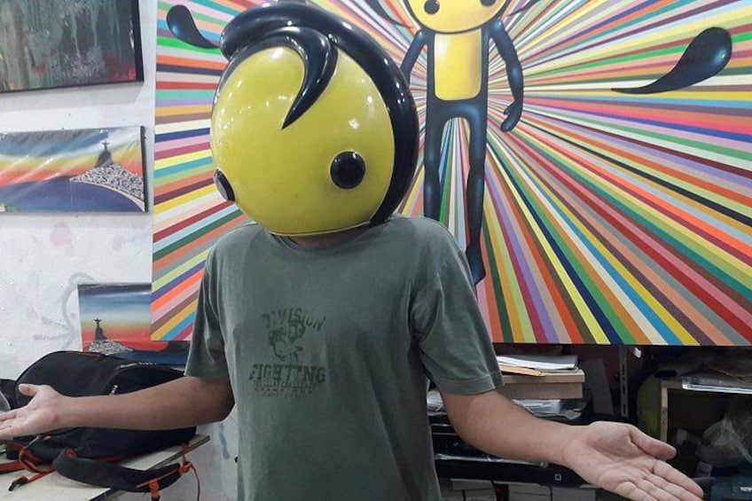 A person wearing a yellow helmet with a black stripe, standing in front of a colorful abstract painting. 3