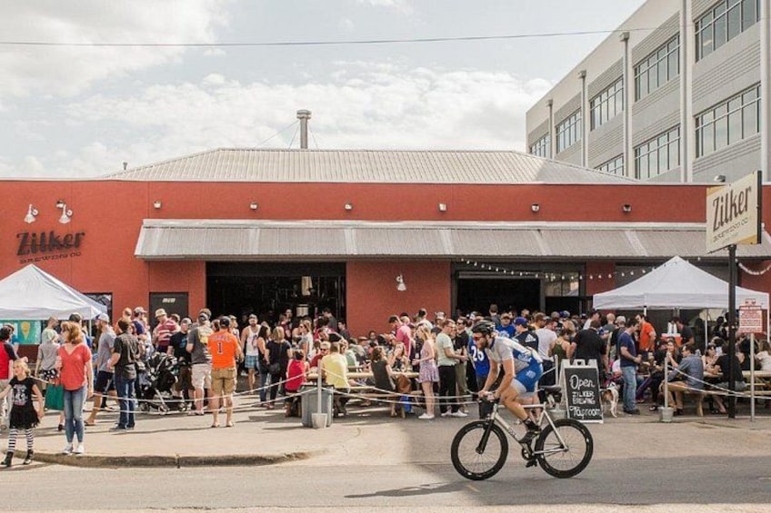 A crowd gathered outside a building with a red facade and a sign that reads 'Zilker.' 2