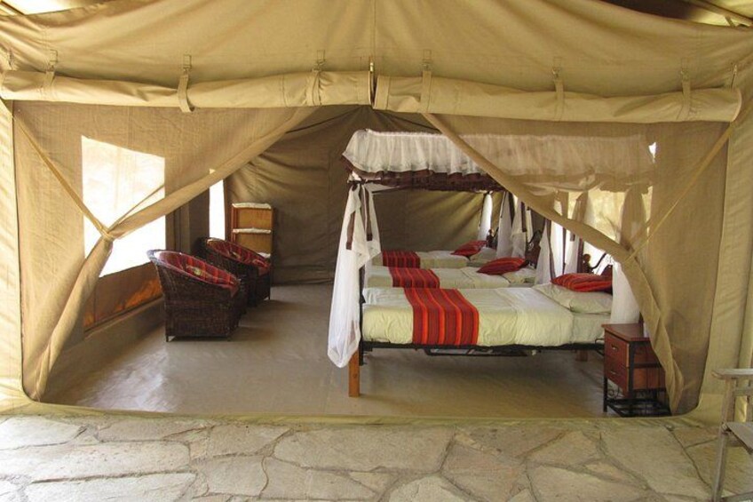 A tent with a bed, two chairs, and a small table. 1
