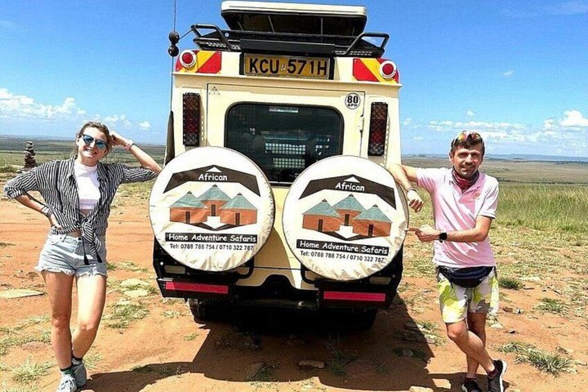 A safari vehicle with 'African Home Adventure Safaris' branding, a desert landscape, and two people posing. 2
