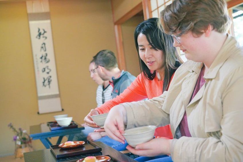 A group of people sitting at a table with bowls and chopsticks, likely engaged in a meal or tea ceremony. 2