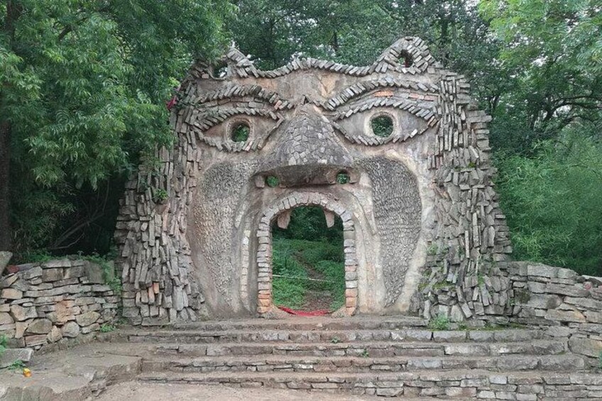 A stone structure resembling a face with eyes and a mouth, surrounded by greenery. 4