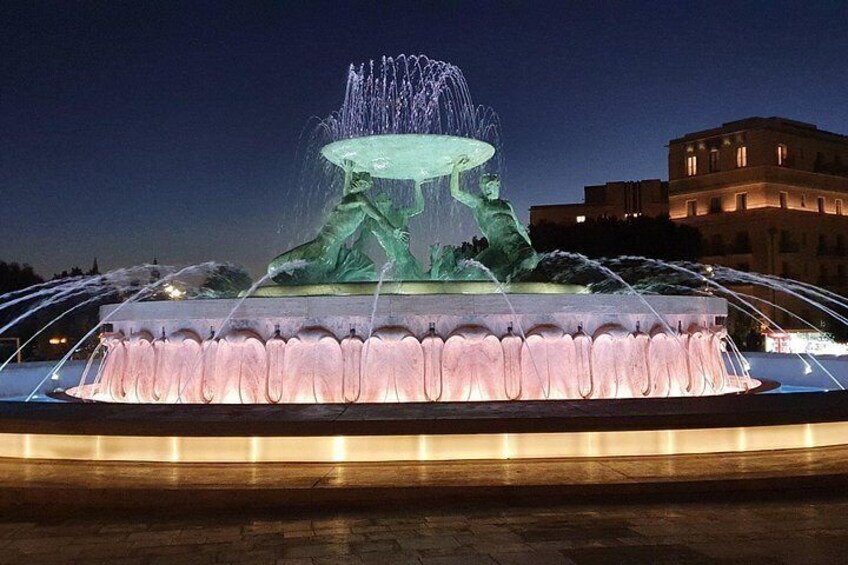 A nighttime illuminated fountain with water jets and a sculpture. 2