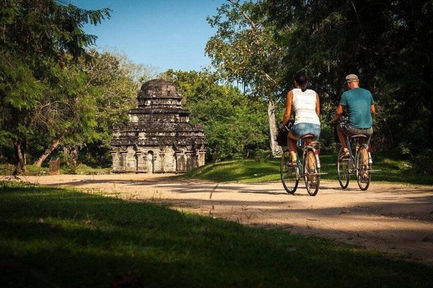 Dos personas montando en bicicleta por un sendero de tierra, con una estructura histórica al fondo. 1