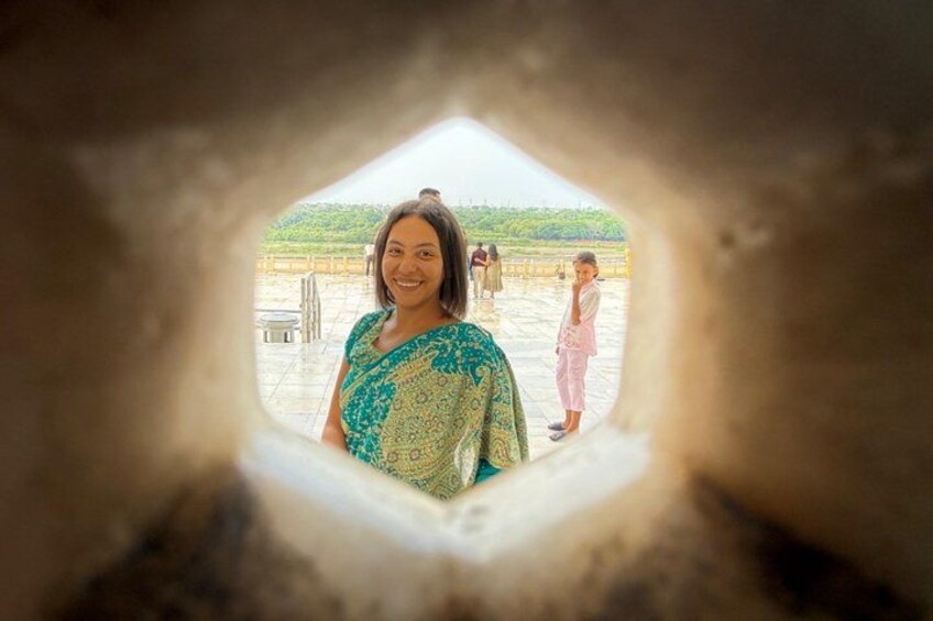 A person standing in a stone structure with a view of a courtyard and other people in the background. 2