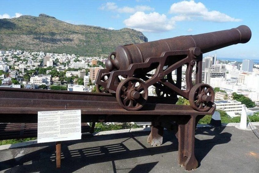 Un cañón grande exhibido, con un paisaje urbano y montañas al fondo. 5