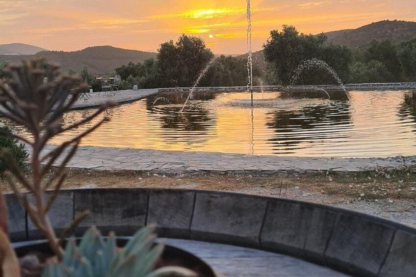 A sunset over a calm lake with fountains, surrounded by hills and a paved walkway. 5