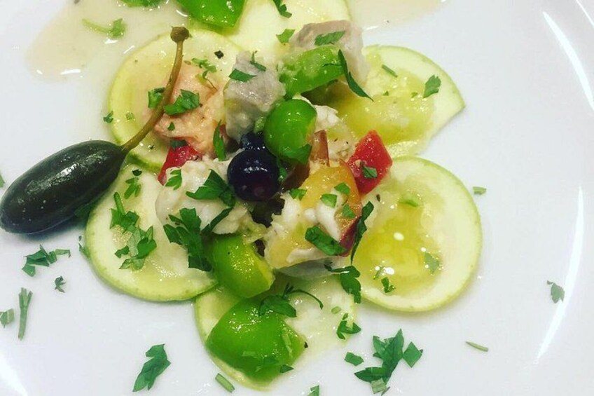 A dish with sliced cucumbers, olives, and herbs on a white plate. 4