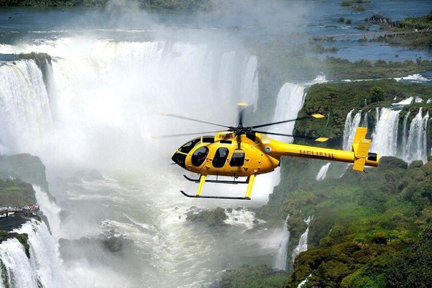 Een gele helikopter vliegt boven een waterval. 1