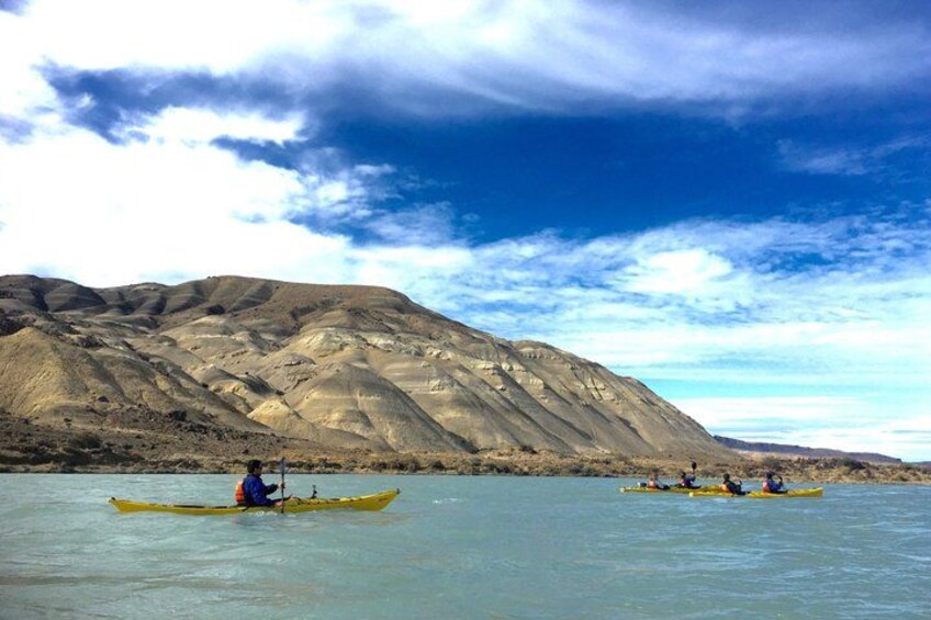 A group of people kayaking on calm water with a mountainous landscape in the background. 1