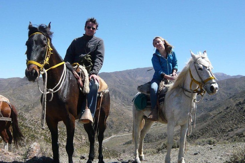 Two people riding horses on a mountain trail. 1