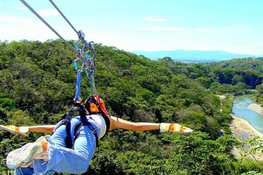Una persona practica puenting con los brazos extendidos, rodeada de un bosque verde denso y un río abajo. 5