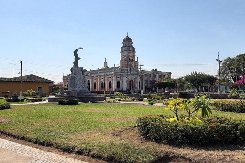A historic building with a bell tower, surrounded by a well-maintained garden with a statue in the foreground. 1
