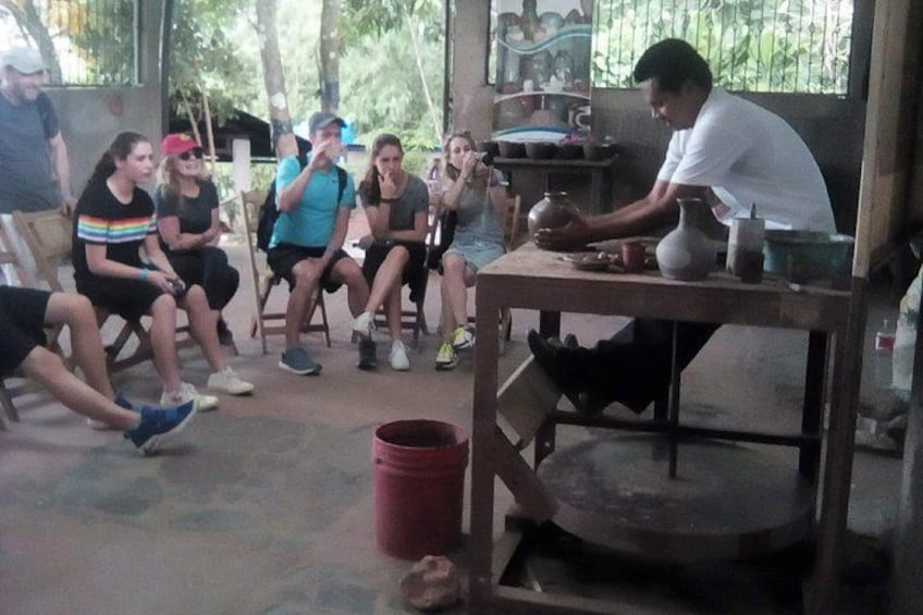 A group of people seated around a pottery wheel, observing a potter shaping clay. 5