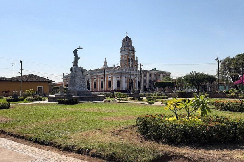 A historic building with a bell tower, surrounded by a well-maintained garden with a statue. 1