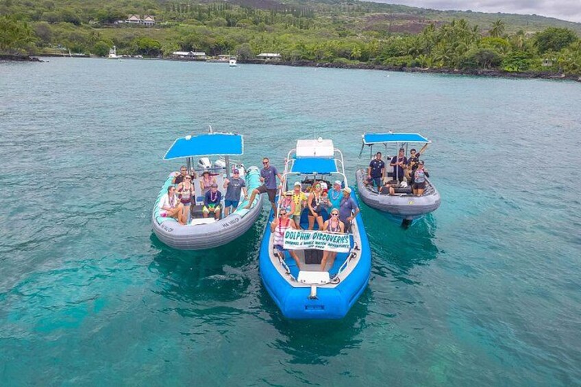 Three boats on turquoise water with people on them, surrounded by greenery and houses in the background. 2