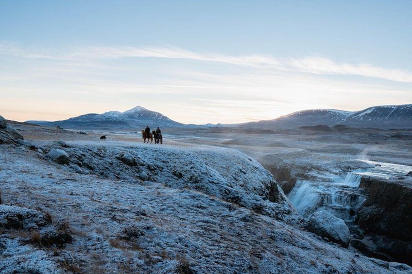 A snowy landscape with a waterfall, mountains, and a group of people in the distance. 5