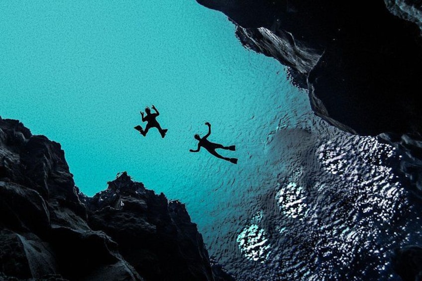 Three divers swimming in a clear blue water body surrounded by rocky cliffs. 4