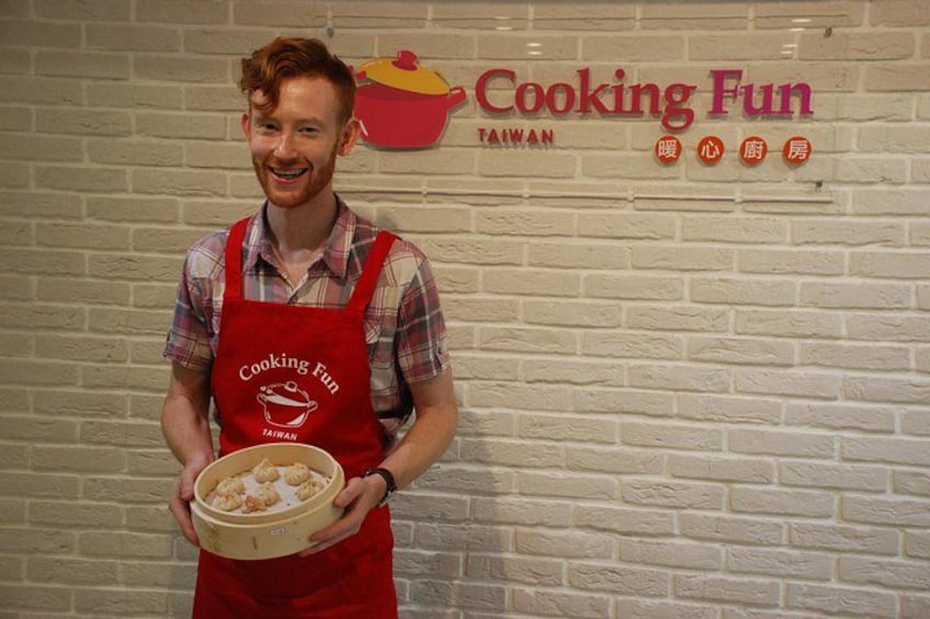 A person holding a bowl of food in front of a wall with a sign that reads 'Cooking Fun Taiwan.' 4