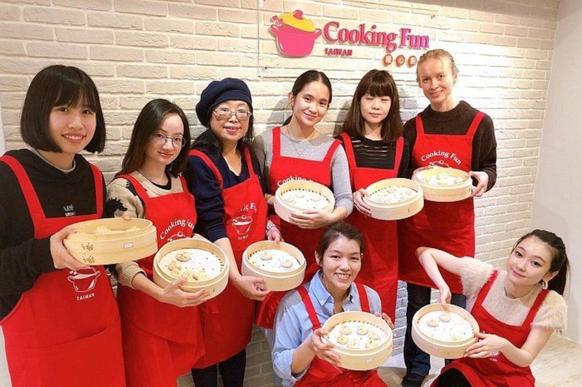 A group of people in red aprons holding round dishes with food, standing in front of a sign that reads 'Cooking Fun Taiwan.' 3