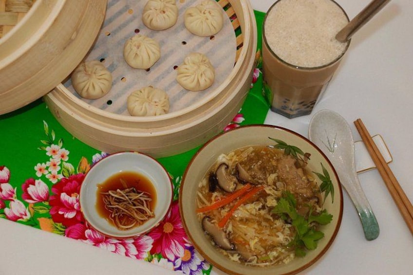 A meal with a bowl of soup, a plate of dumplings, a cup of tea, and a spoon. 2