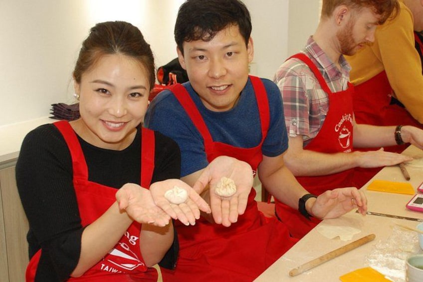 People wearing red aprons, holding dough, and working with baking tools. 1