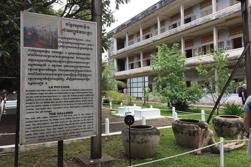 Un edificio histórico con una cartelera, mesas al aire libre y grandes macetas. 4