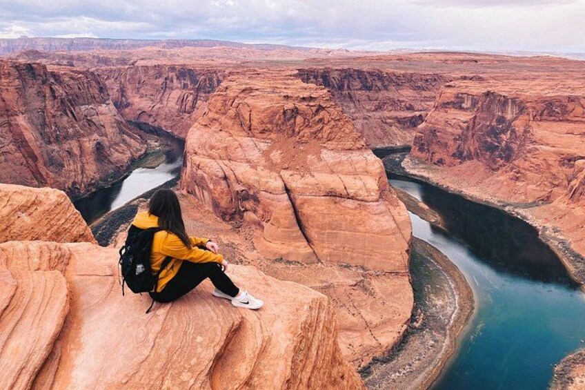 Una persona sentada en un saliente rocoso, contemplando un cañón con un río. 1