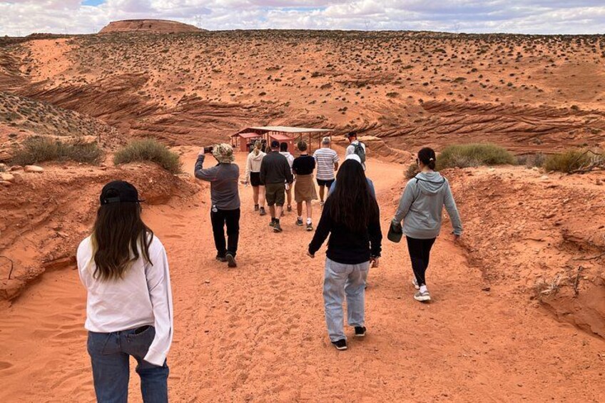 Un grupo de personas caminando por un sendero rojizo en un paisaje desértico con vegetación escasa y una colina al fondo. 3
