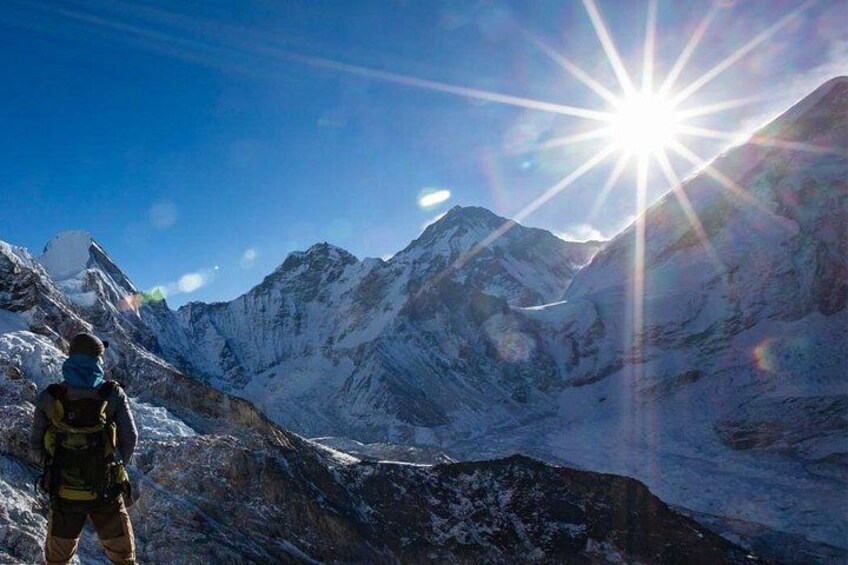 Una persona de pie en una montaña nevada con un sol brillante al fondo. 1