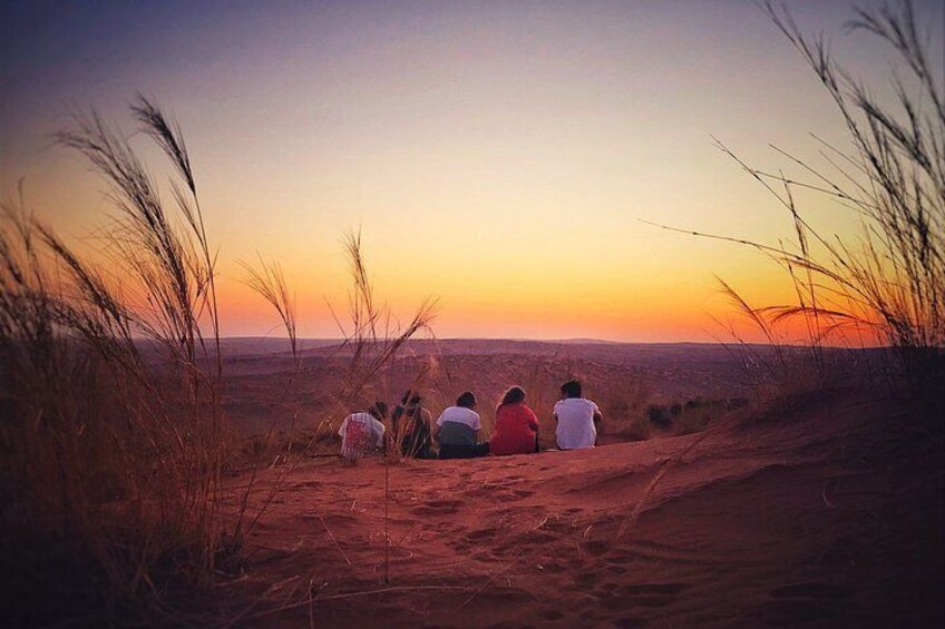 A group of people sitting on a sandy dune at sunset. 3