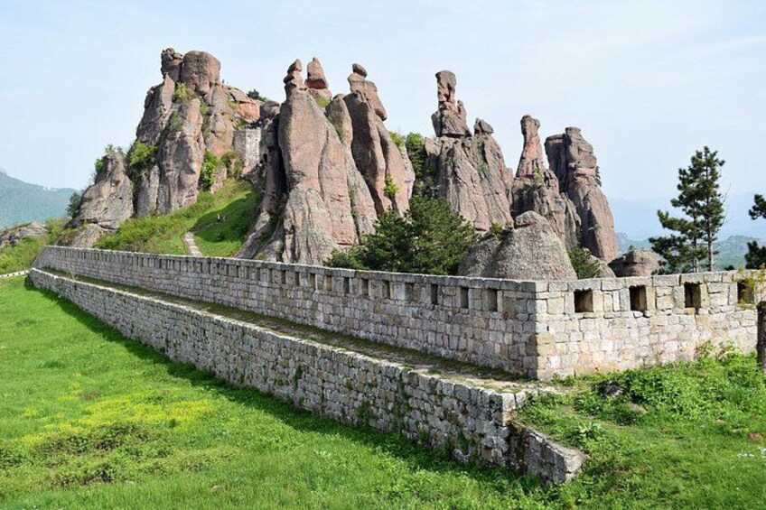 Un mur de pierres menant à un sommet montagneux rocheux, sous un ciel dégagé. 2
