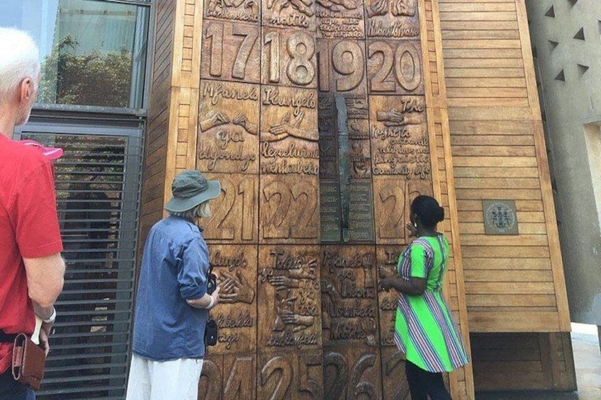 En trævæg med indgraverede tal og tekst, en ståldør og en bygning med en geometrisk facade. 4