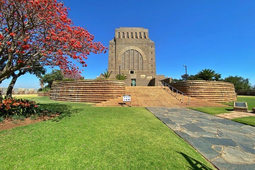 A large stone building with a central arched window, surrounded by a circular stone wall and a grassy area with a tree. 2