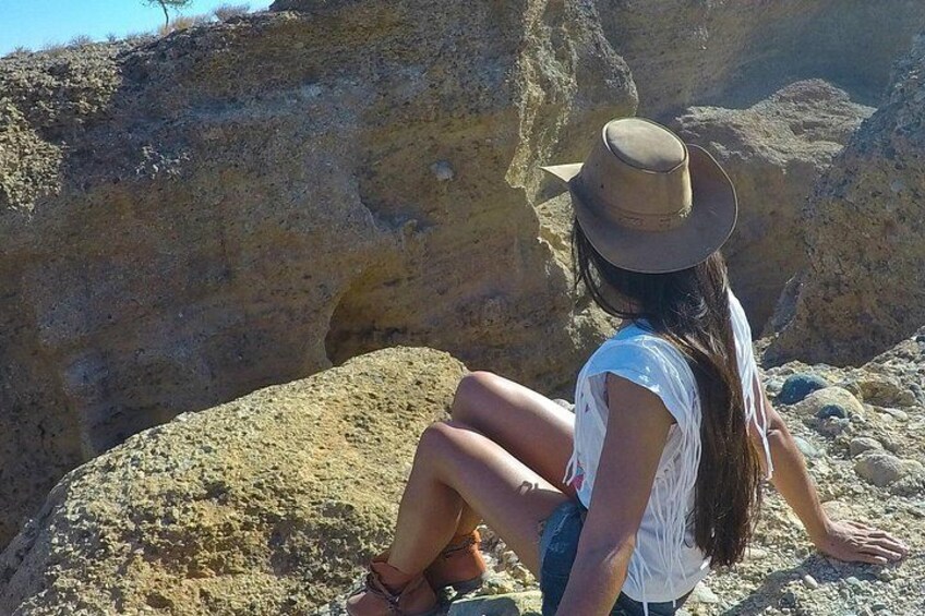 A person sitting on a rock with a hat, surrounded by a rocky landscape. 2