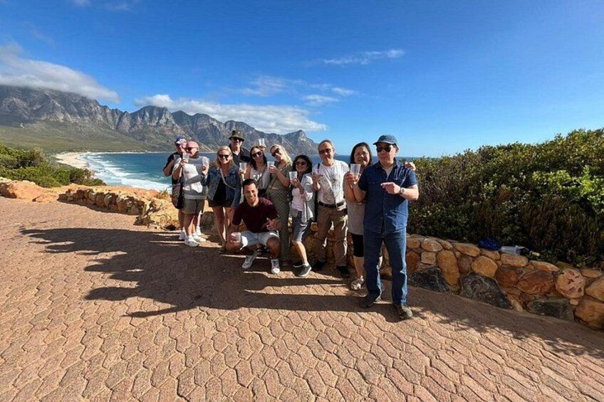 A group of people posing on a paved walkway with a coastal landscape in the background. 4