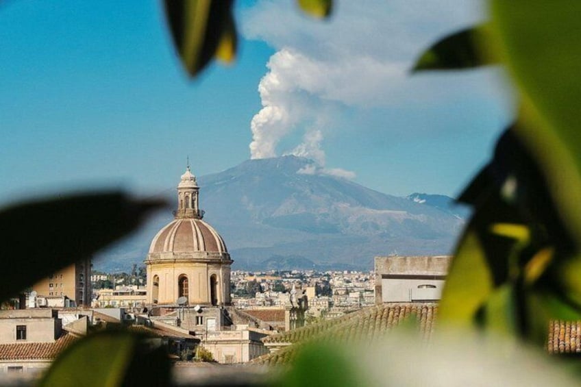 A cityscape with a prominent dome-shaped building, a volcano in the background, and a clear sky. 1