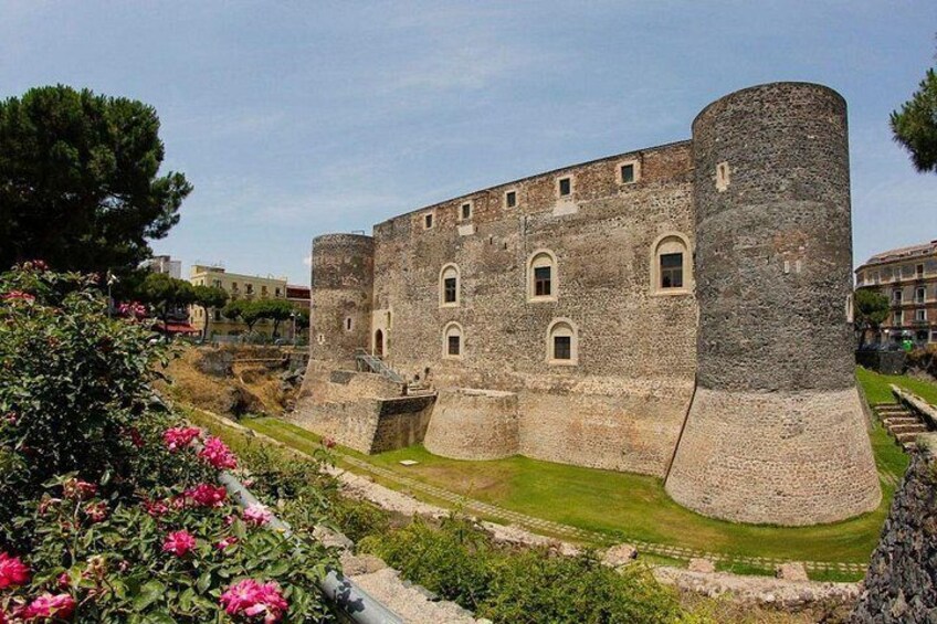 A historic stone castle with a large round tower, surrounded by well-maintained gardens and a clear sky. 3