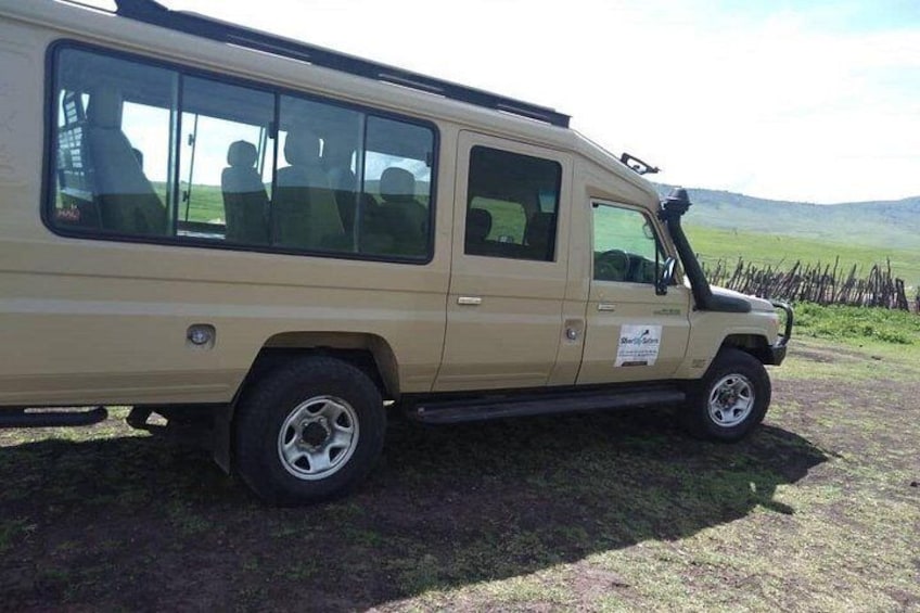 A beige off-road vehicle parked on a grassy field with a fence in the background. 1