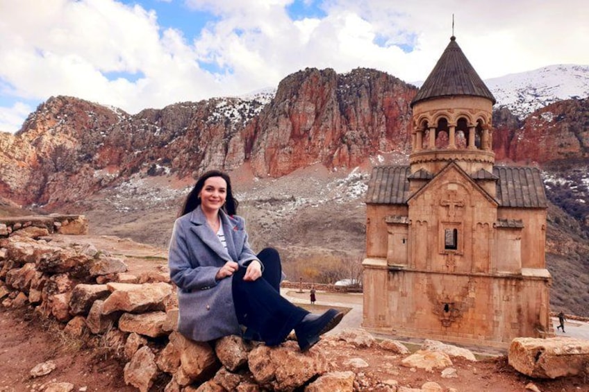 Una persona seduta su delle rocce, con una piccola chiesa e montagne impervie sullo sfondo. 3